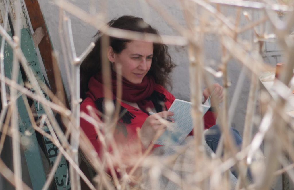 Autorin Tala T. Alsted schreibt (versteckt hinter Pflanzen) in ein Notizbuch