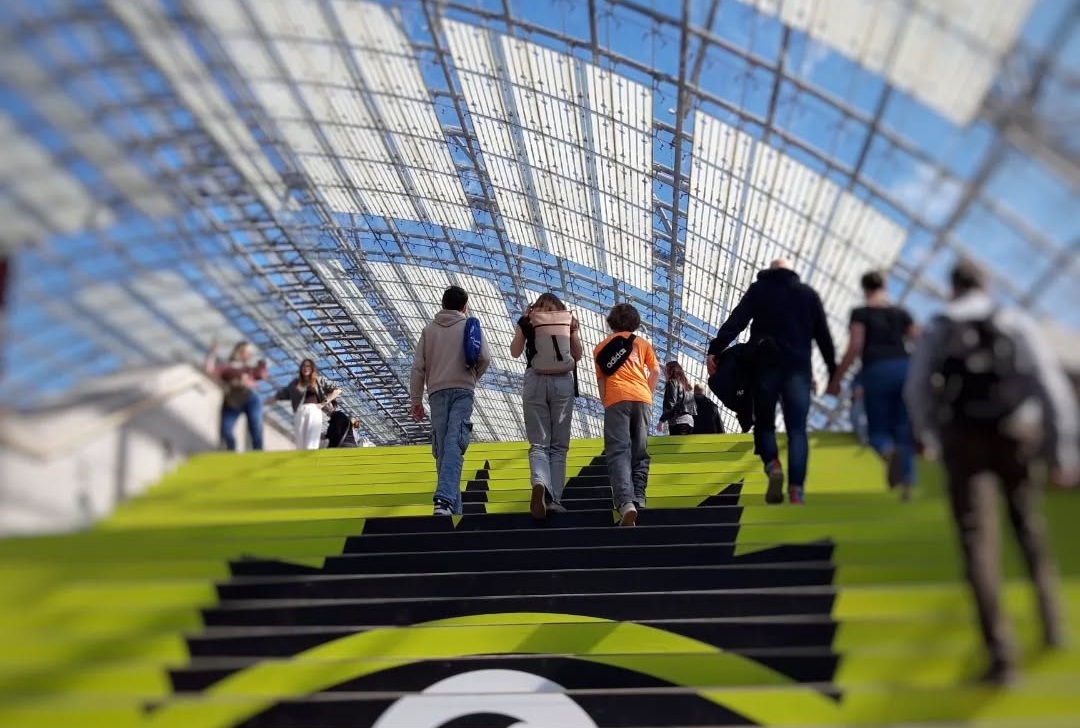 Menschen gehen die grün beklebten Stufen in der Glashalle der Leipziger Messe hoch.